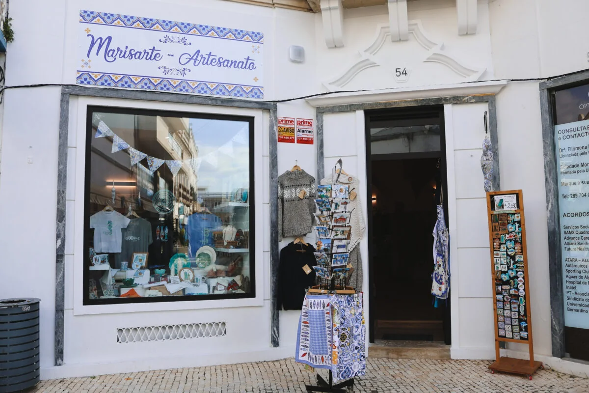 A fachada branca da Marisarte, com o letreiro azul «Marisarte – Artesanato» e a montra